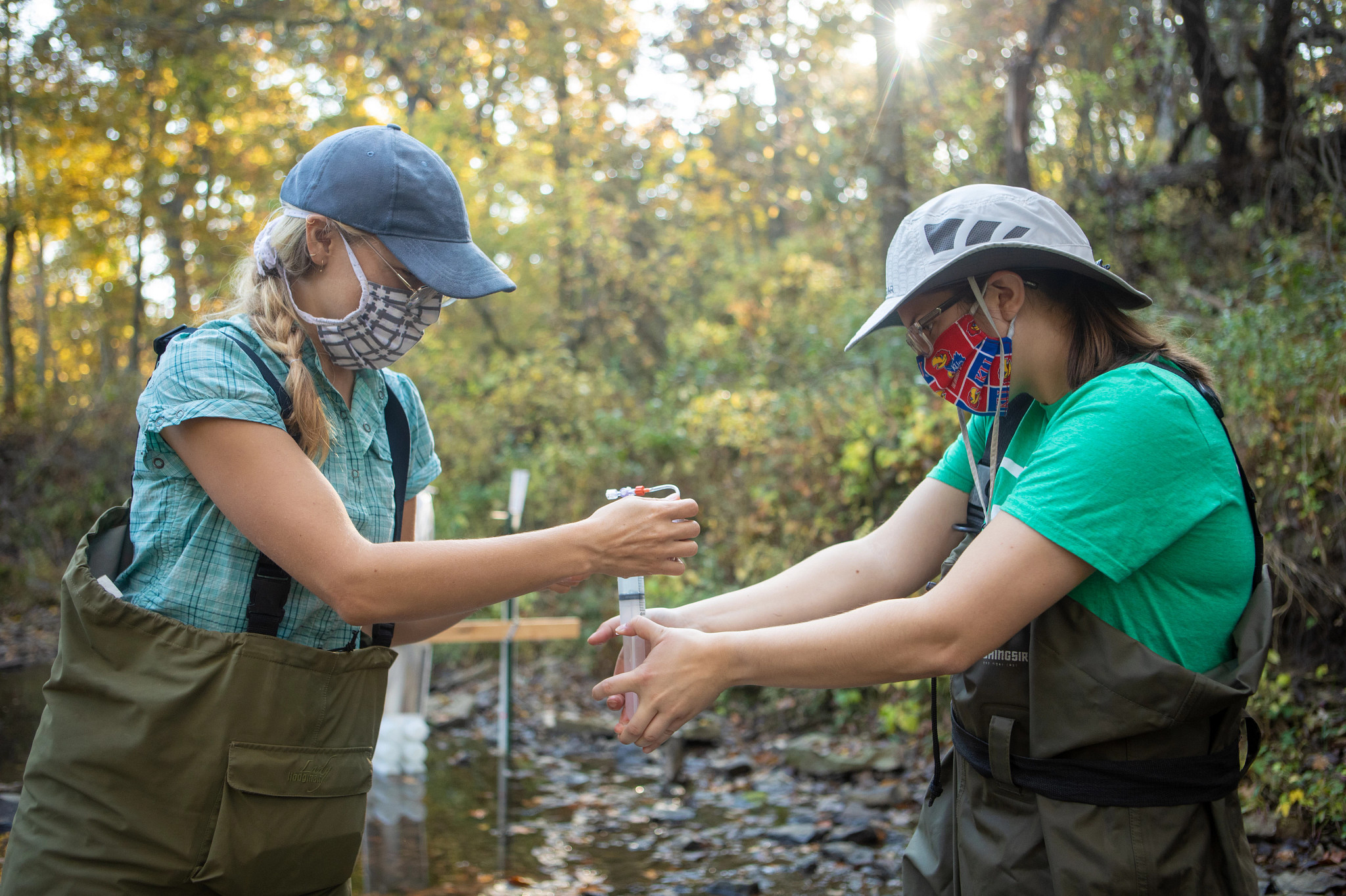 two students in waders collect samples from a river bed