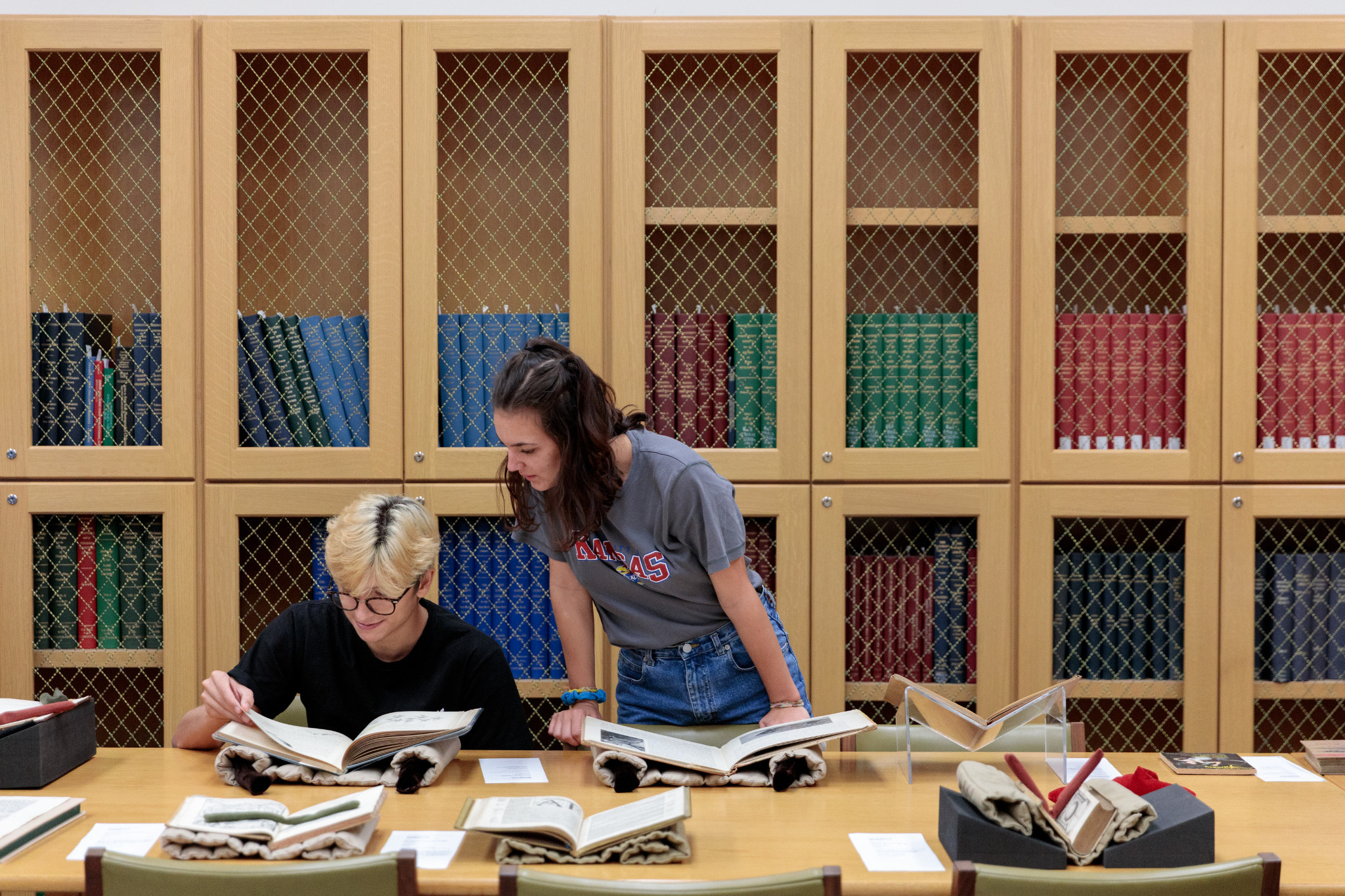 two students examine texts in front of shelves of books