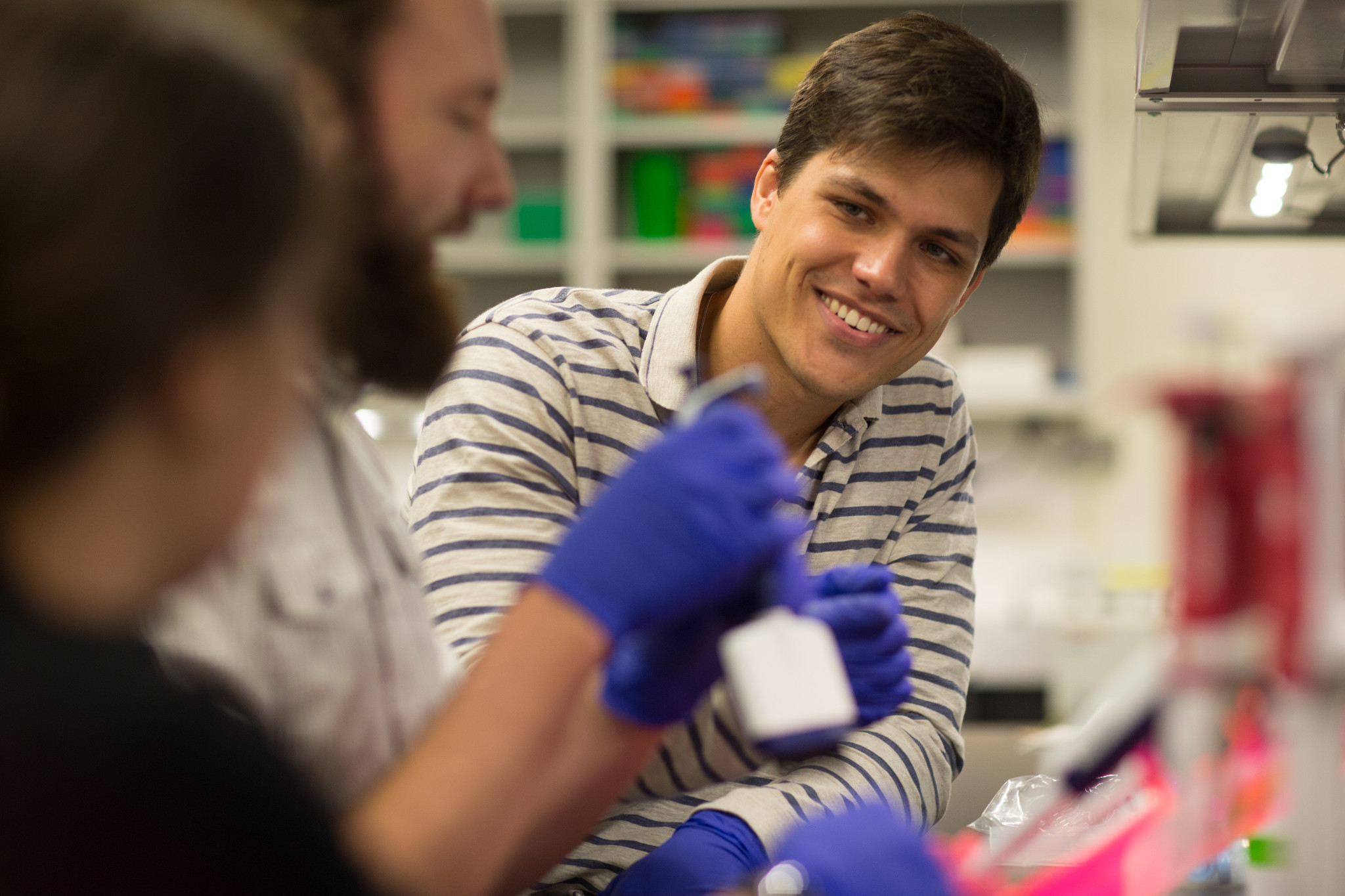 student in striped shirt smiles at partners in lab setting