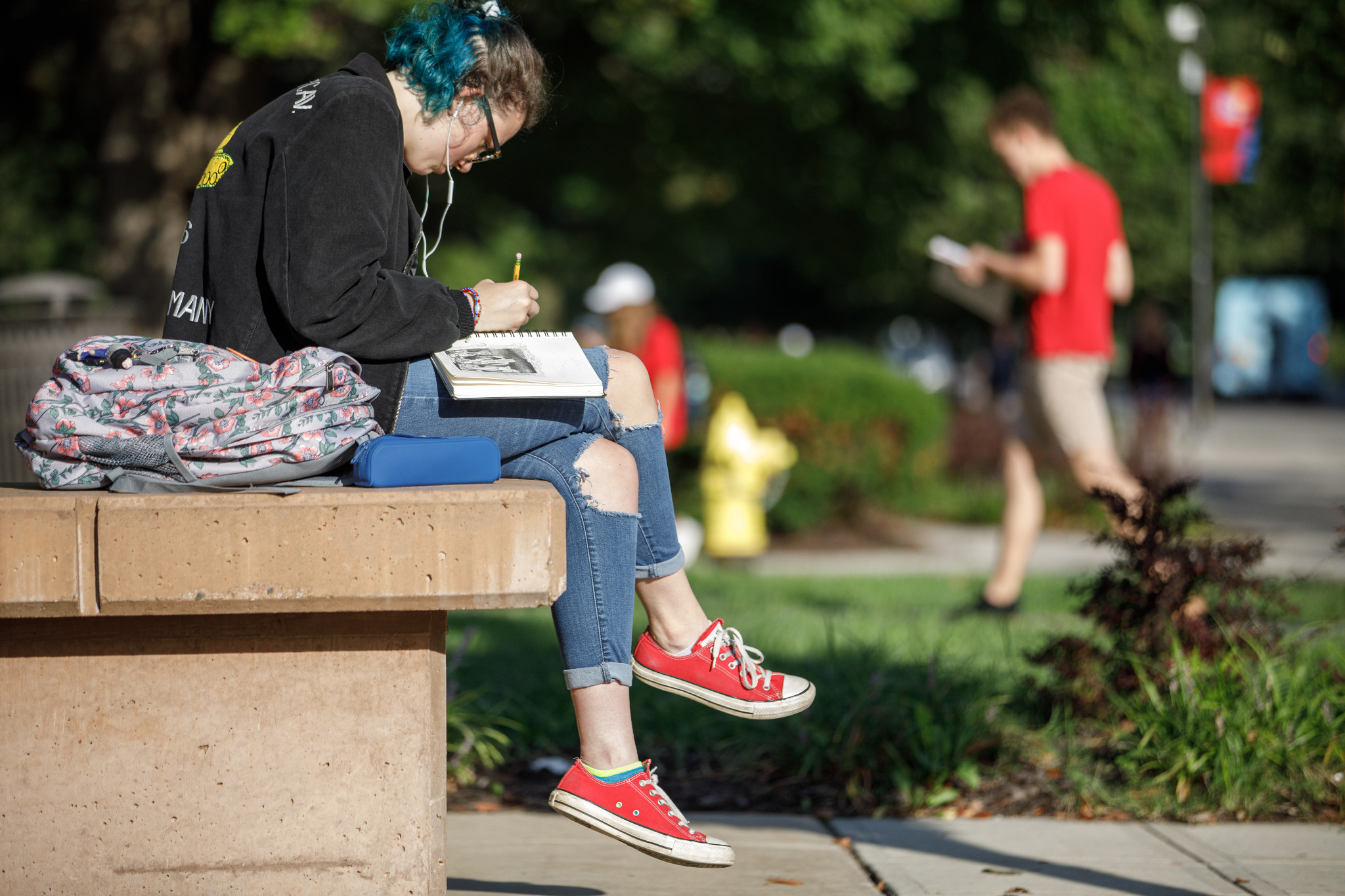 student in black sweatshirt jeans and red shoes studies on bench