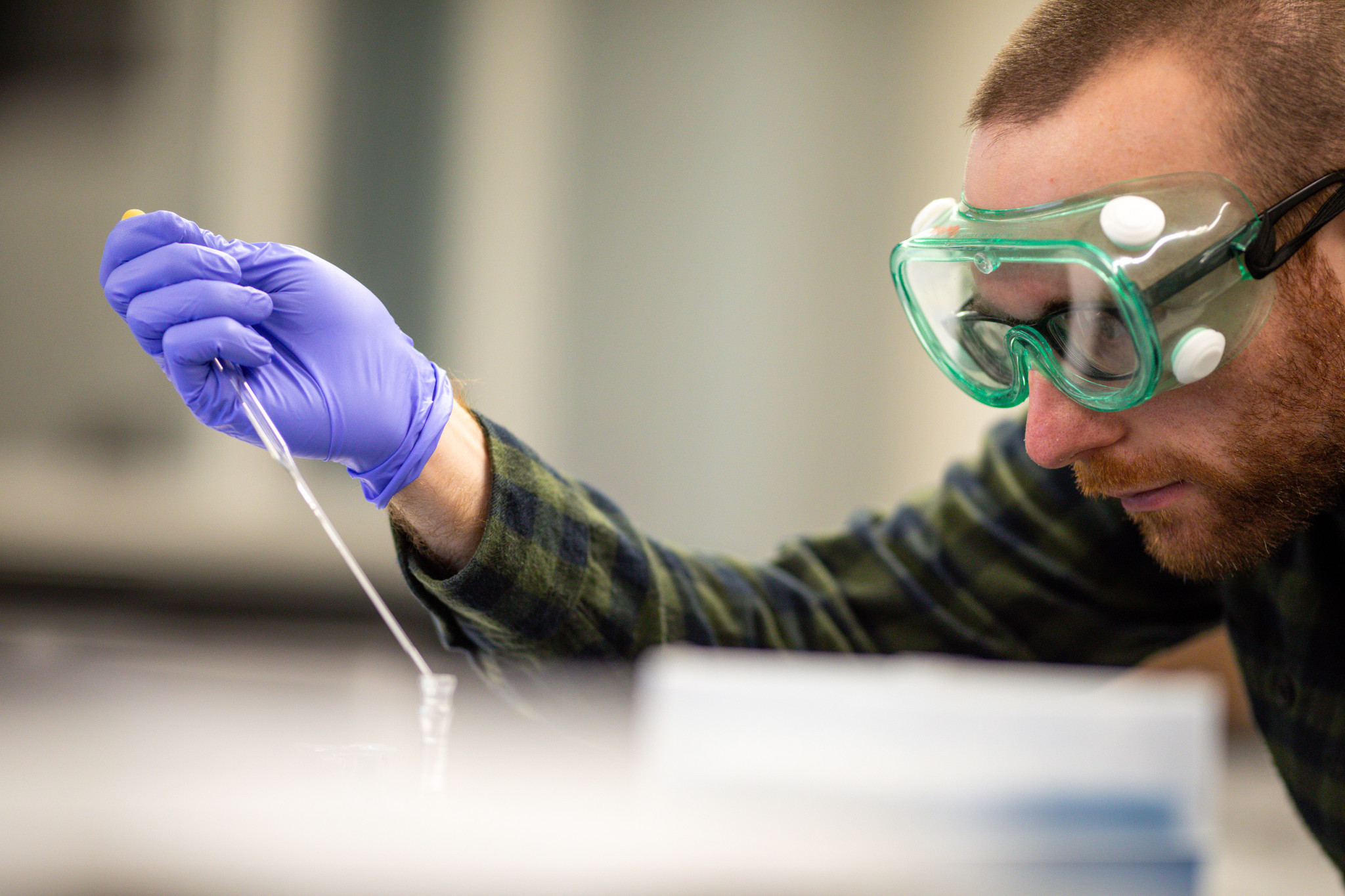 student in lab goggles puts pipette into test tube