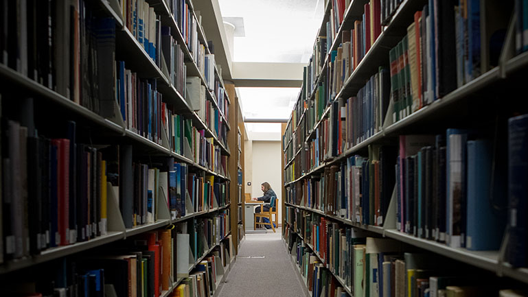 shot looking down isle of library with a student studying at a table at the end